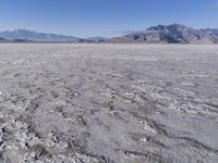 a wide expanse of land with low mountain and sky background, showing blue sky, mountains, and a few large patches of white cloudy dirt