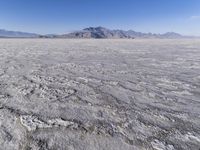 a wide expanse of land with low mountain and sky background, showing blue sky, mountains, and a few large patches of white cloudy dirt