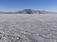 a wide expanse of land with low mountain and sky background, showing blue sky, mountains, and a few large patches of white cloudy dirt