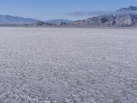 a wide expanse of land with low mountain and sky background, showing blue sky, mountains, and a few large patches of white cloudy dirt