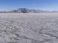 a wide expanse of land with low mountain and sky background, showing blue sky, mountains, and a few large patches of white cloudy dirt