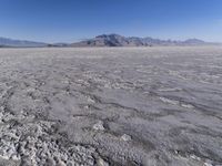 a wide expanse of land with low mountain and sky background, showing blue sky, mountains, and a few large patches of white cloudy dirt
