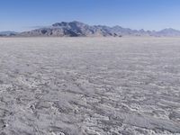 a wide expanse of land with low mountain and sky background, showing blue sky, mountains, and a few large patches of white cloudy dirt