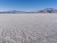 a wide expanse of land with low mountain and sky background, showing blue sky, mountains, and a few large patches of white cloudy dirt