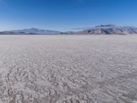 a wide expanse of land with low mountain and sky background, showing blue sky, mountains, and a few large patches of white cloudy dirt