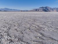a wide expanse of land with low mountain and sky background, showing blue sky, mountains, and a few large patches of white cloudy dirt