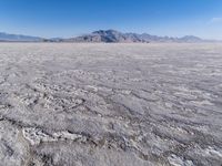 a wide expanse of land with low mountain and sky background, showing blue sky, mountains, and a few large patches of white cloudy dirt