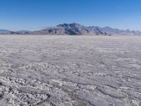 a wide expanse of land with low mountain and sky background, showing blue sky, mountains, and a few large patches of white cloudy dirt