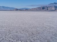 a wide expanse of land with low mountain and sky background, showing blue sky, mountains, and a few large patches of white cloudy dirt