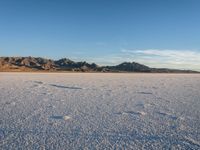 a person walks across a wide open expanse covered in snow and rocks, next to mountains and clouds