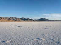 a person walks across a wide open expanse covered in snow and rocks, next to mountains and clouds