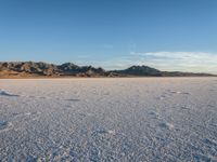 a person walks across a wide open expanse covered in snow and rocks, next to mountains and clouds