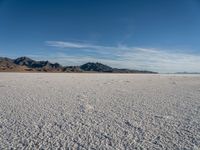a person walks across a wide open expanse covered in snow and rocks, next to mountains and clouds