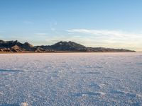 a person walks across a wide open expanse covered in snow and rocks, next to mountains and clouds