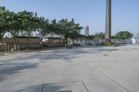 a wide paved parking space and trees with the water in the background and people walking next to it