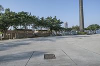 a wide paved parking space and trees with the water in the background and people walking next to it