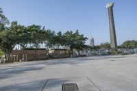 a wide paved parking space and trees with the water in the background and people walking next to it