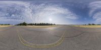 a panoramic view of a wide open road and trees in the distance with clouds overhead