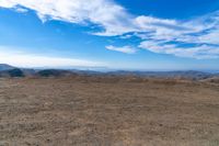 a wide view of mountains and a sky with clouds over them from a dirt field