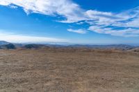 a wide view of mountains and a sky with clouds over them from a dirt field