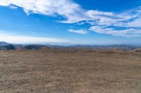 a wide view of mountains and a sky with clouds over them from a dirt field