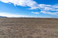 a wide view of mountains and a sky with clouds over them from a dirt field