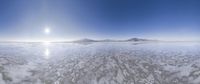 a wide view of the sun in a cloudy sky over the ocean with a snow covered shoreline