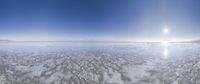 a wide view of the sun in a cloudy sky over the ocean with a snow covered shoreline