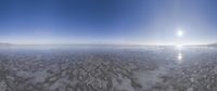 a wide view of the sun in a cloudy sky over the ocean with a snow covered shoreline