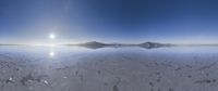 a wide view of the sun in a cloudy sky over the ocean with a snow covered shoreline