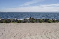 a brick path between two rocks near a beach and the ocean is very wide water