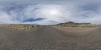 a big wide angle image of a road going through a desert area under a cloudy sky