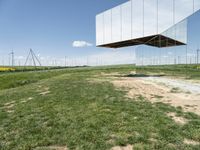 a large mirror structure in a field with wind turbines in the background behind it and a blue sky above