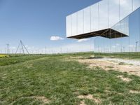 a large mirror structure in a field with wind turbines in the background behind it and a blue sky above