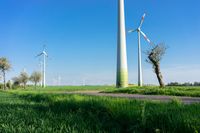 many wind turbines in the grass with trees near by in the background of clear blue sky