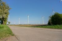 a row of wind turbines on a dirt road in front of a green field and trees