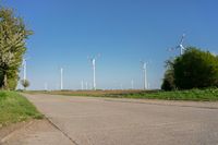 a row of wind turbines on a dirt road in front of a green field and trees