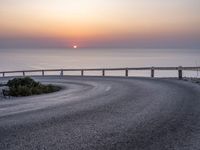 a winding curve near the ocean at sunset on a road between two lakes with bridge leading to water