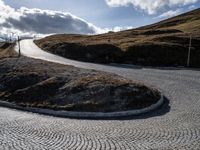 the circular gravel road that winds up at the end of a steep slope that is dotted with pavement and has bushes around the edge,