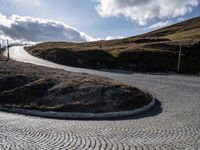 the circular gravel road that winds up at the end of a steep slope that is dotted with pavement and has bushes around the edge,