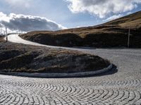 the circular gravel road that winds up at the end of a steep slope that is dotted with pavement and has bushes around the edge,