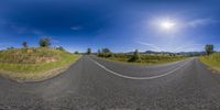 a road that is winding toward the sun through some grass, mountains, and trees