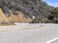 the road is winding along the mountain side with trees on it and one vehicle driving down the hill