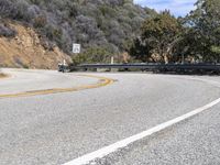 the road is winding along the mountain side with trees on it and one vehicle driving down the hill