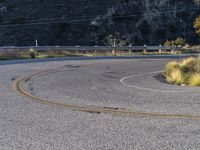 a road sign sitting on the side of a winding curvy road near a mountain