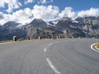 the paved road is winding off into the distance in front of the mountains under a blue sky with white clouds