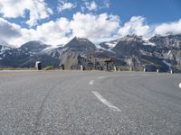 the paved road is winding off into the distance in front of the mountains under a blue sky with white clouds