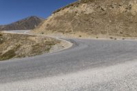 a winding road goes through the mountains on an empty mountain side, with a single motorcycle in the middle