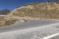 a winding road goes through the mountains on an empty mountain side, with a single motorcycle in the middle