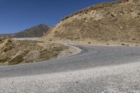 a winding road goes through the mountains on an empty mountain side, with a single motorcycle in the middle